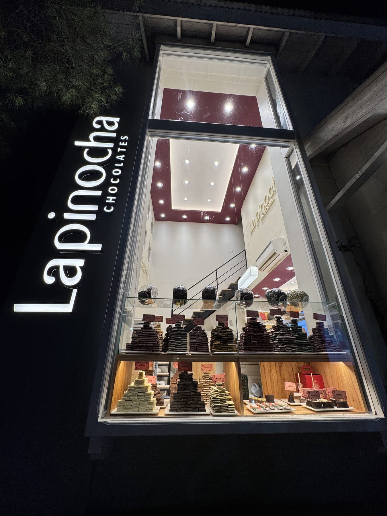 Local La Pinocha Chocolates a la calle, de noche, con clientes en la vereda